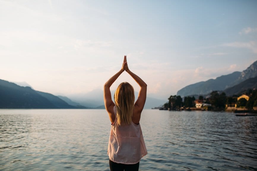 A woman in the yoga "tree pose" in front of a vast lake.
