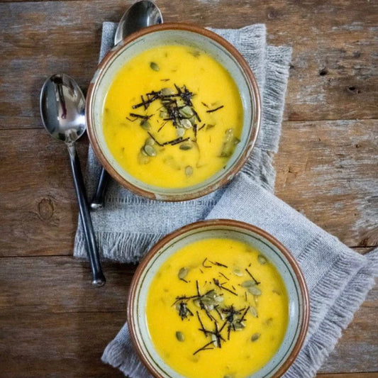 Two bowls of golden turmeric or butternut squash soup garnished with seeds and herbs on a rustic wooden surface with linen napkin and spoon Two bowls of golden turmeric or butternut squash soup garnished with seeds and herbs on a rustic wooden surface with linen napkin and spoon