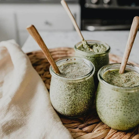 Three jars of chia pudding with wooden spoons on a woven tray in a kitchen setting. Three jars of chia pudding with wooden spoons on a woven tray in a kitchen setting.
