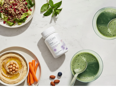 Healthy food items including a salad, hummus, carrots, nuts, and a bottle of Clean Shine supplement on a white surface.