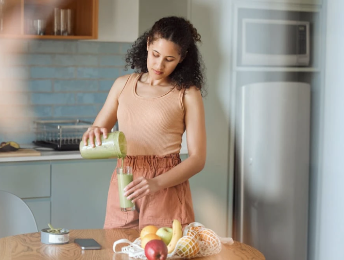 Woman pouring Matcha smoothie from blender into a glass