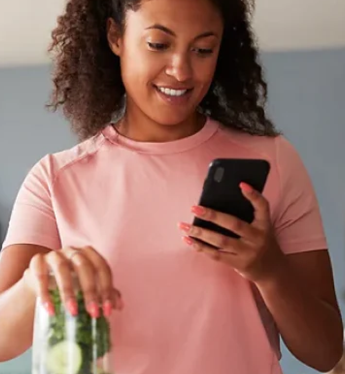 Woman checks her phone while making a smoothie with a blender, clean health coaching