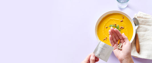 Person holding a Clean 7 supplement package with a bowl of soup on a table