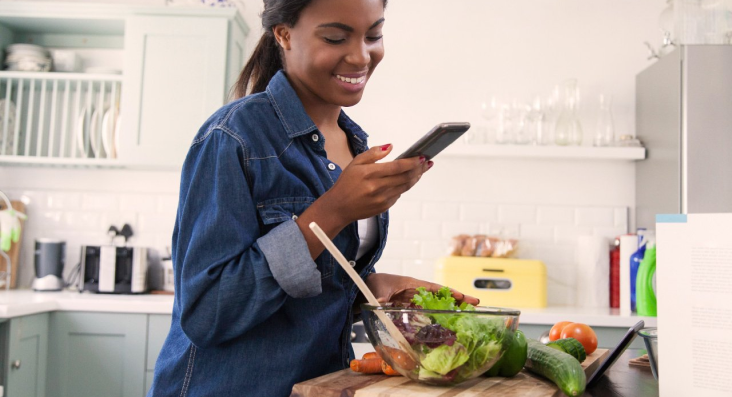 Woman preparing a salad and checking her cell phone
