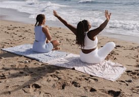 Two women sitting on a towel watching the water on the beach