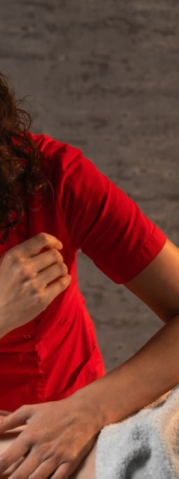 A masseuse in a red shirt applies her elbow in a massage to a male person’s back, who is likely wondering what toxins are released after a massage like this.
