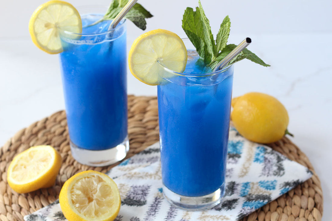 Blue mocktails with slices of lemon in a clear glass sitting on top of a napkin
