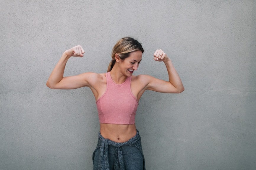 woman in a pint tank top flexing with a grey background