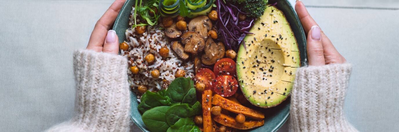 A young woman in a sweater holding a bowl of healthy metabolism boosting whole foods
