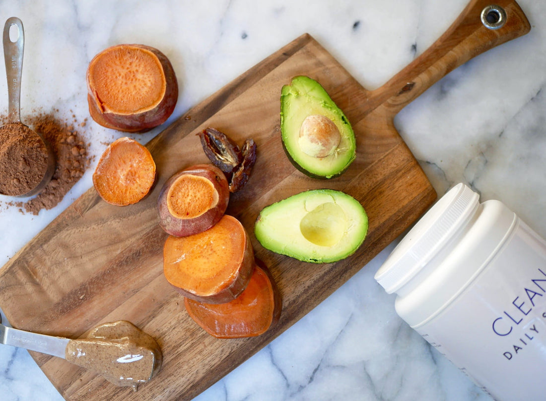 Cacao powder, sweet potatoes and avocado on a cutting board next to a clean product canister