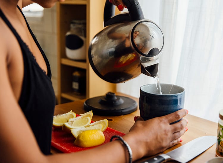 Woman pouring hot water into a mug with lemons next o her on a table