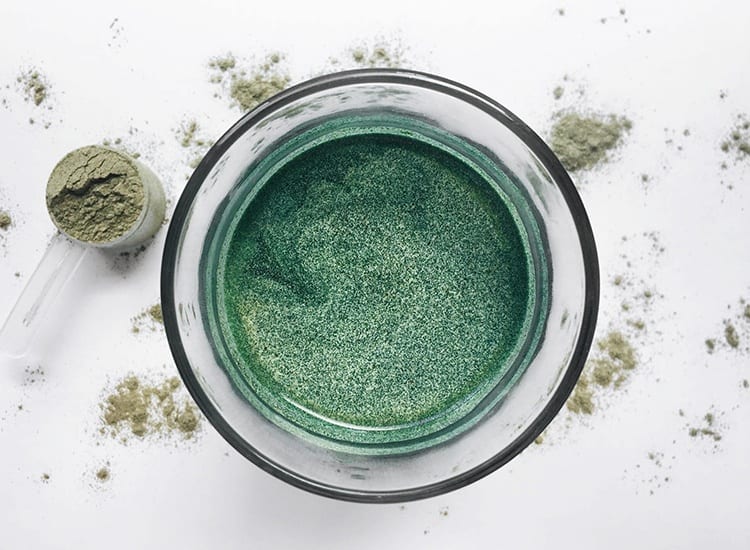 green drink in a glass with a scoop holding green powder on the counter next to it