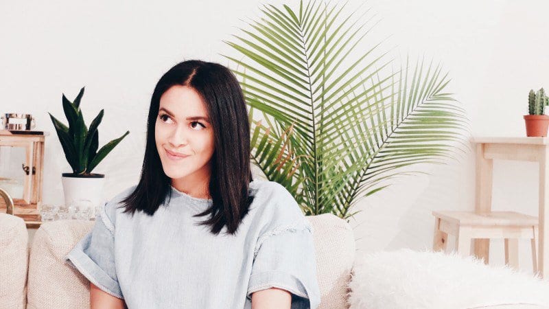 woman thinking and smiling while sitting in a living room on a couch with house plants in the background