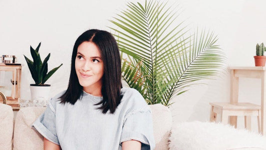 woman thinking and smiling while sitting in a living room on a couch with house plants in the background