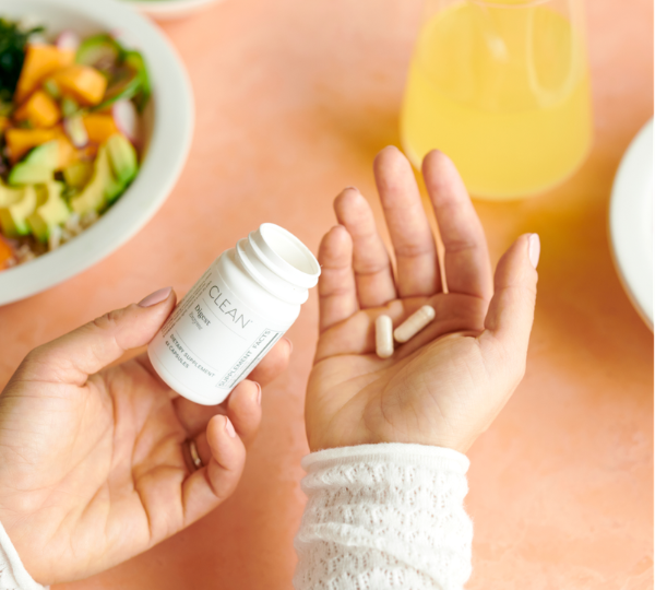 Person holding a Digest supplement bottle with pills in their hand, surrounded by a salad and orange juice.