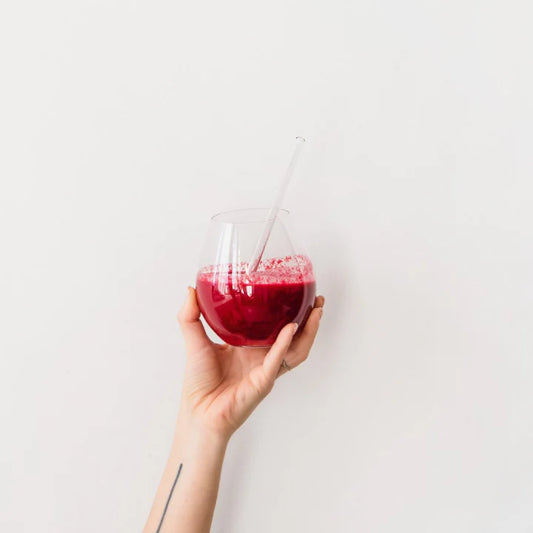 Hand holding a glass of red juice with a straw against a white background