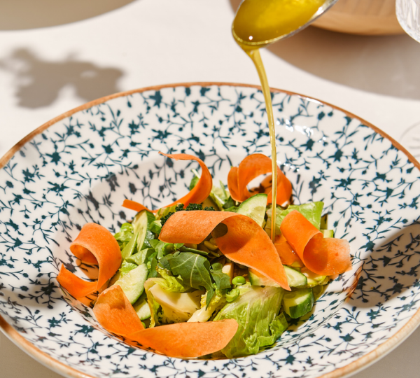 Salad with carrot slices on a decorative plate, drizzled with a liquid, likely olive oil.