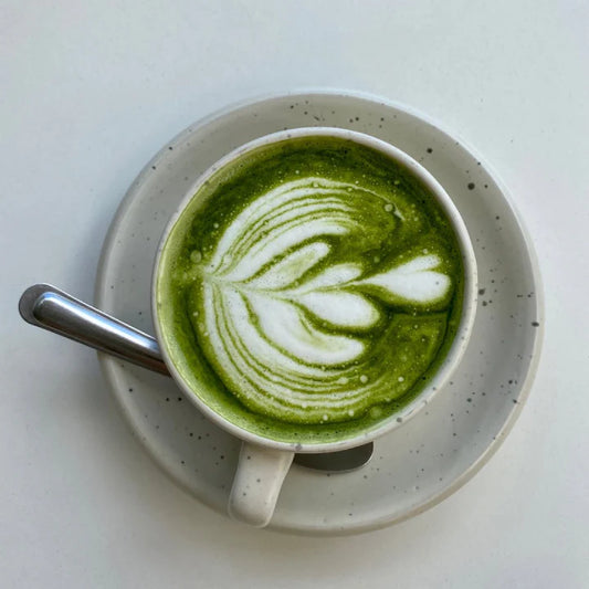 Cup of green matcha latte with leaf design on a white background