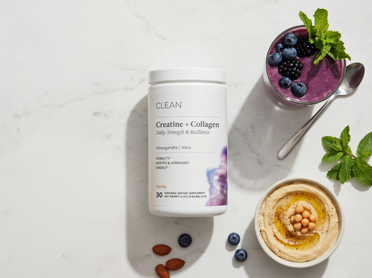 Supplement container labeled 'Clean Creatine + Collagen' with a bowl of hummus, berries, and a smoothie on a light surface.