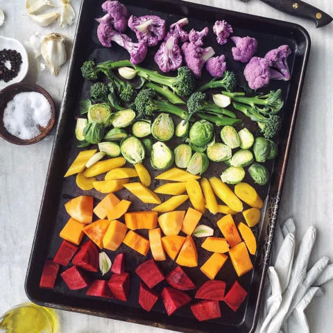 Colorful assortment of vegetables on a baking tray with garlic and salt in the background.