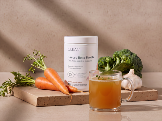 Savory Bone Broth jar with a glass mug, carrots, broccoli, and garlic on stone.