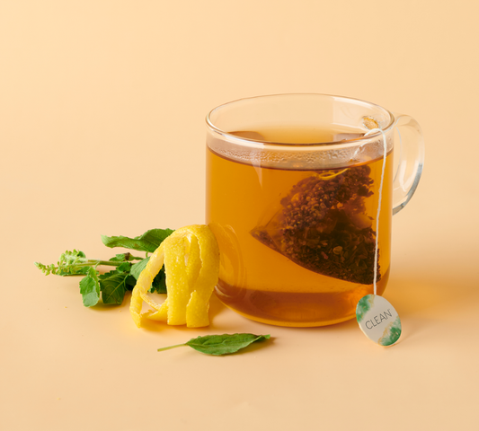 Clear glass mug with hot tea, lemon slice, and tea bag on a beige background